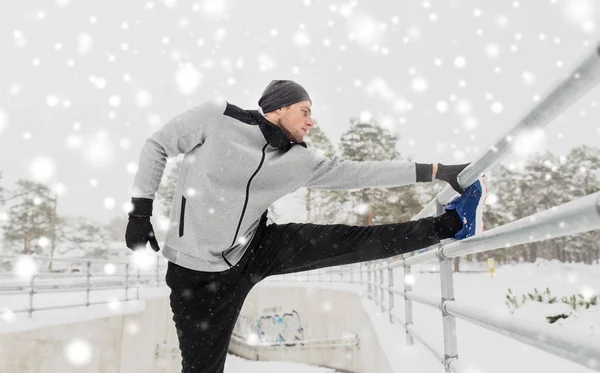 Sports man stretching leg at fence in winter — Stock Photo, Image