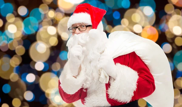 Santa claus with gifts bag over christmas lights — Stock Photo, Image