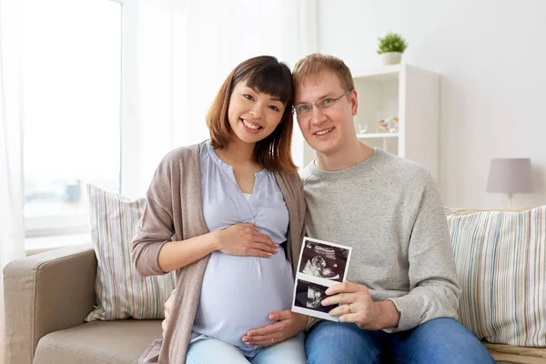 Feliz pareja con imágenes de ultrasonido en casa —  Fotos de Stock