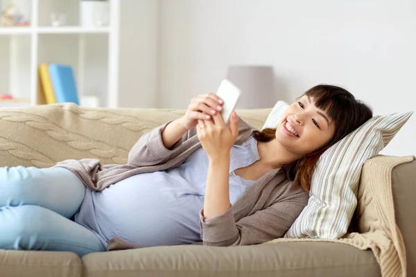 Щаслива вагітна жінка зі смартфоном вдома — стокове фото