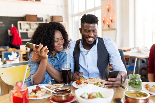 Hombre y mujer felices con teléfonos inteligentes en el restaurante —  Fotos de Stock