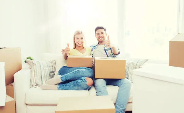 Casal feliz com caixas mostrando polegares para cima em casa — Fotografia de Stock