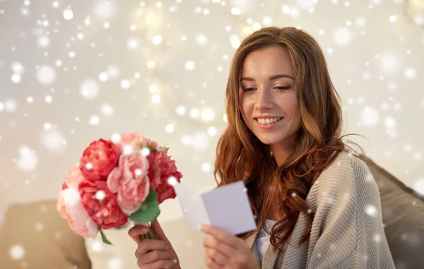 Mulher feliz com flores e cartão de saudação em casa — Fotografia de Stock