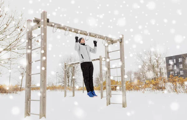 Joven ejercitándose en la barra horizontal en invierno — Foto de Stock