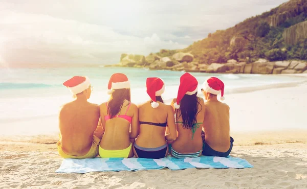 Friends in santa hats on beach at christmas — Stock Photo, Image