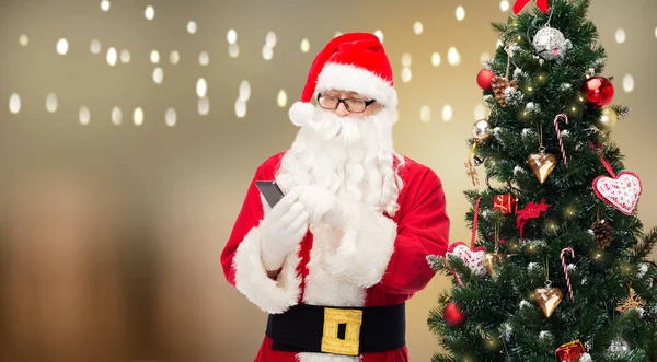 Santa claus com smartphone na árvore de natal — Fotografia de Stock