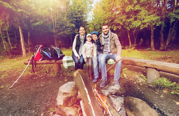 Familia feliz sentado en el banco en el fuego del campamento —  Fotos de Stock