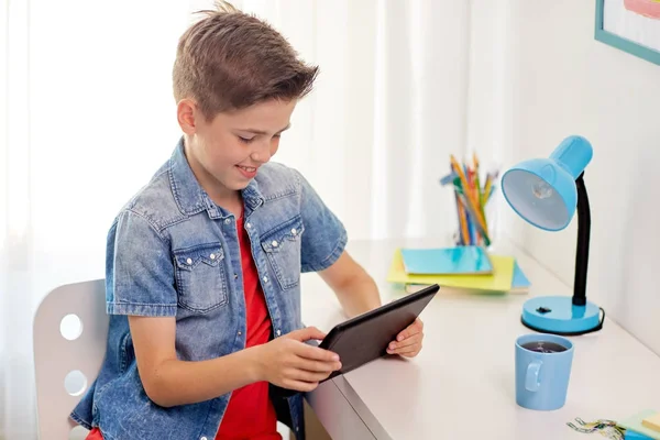Улыбчивый мальчик с планшетным компьютером, сидящий за домашним столом — стоковое фото