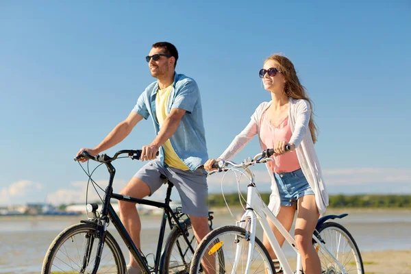 Glada unga par ridning cyklar på seaside — Stockfoto