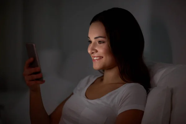 Boldog fiatal nő az ágyban éjjel smartphone — Stock Fotó
