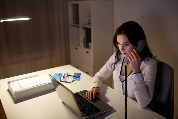 Женщина с ноутбуком звонит по телефону в ночном офисе — стоковое фото