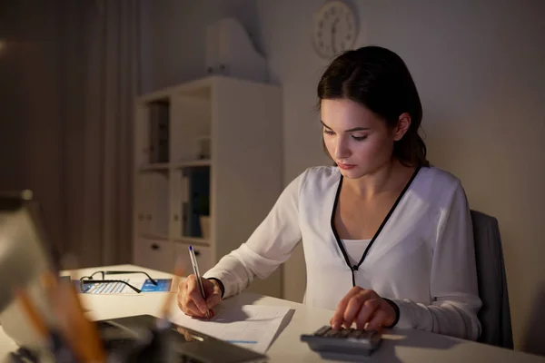 Femme avec calculatrice et papiers au bureau de nuit — Photo