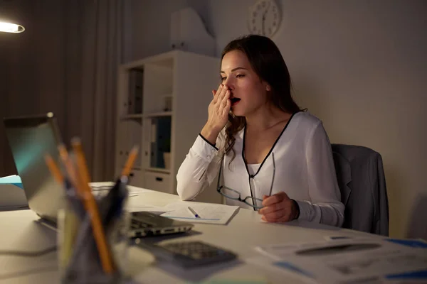 Усталая женщина с бумагами зевает в ночном офисе — стоковое фото