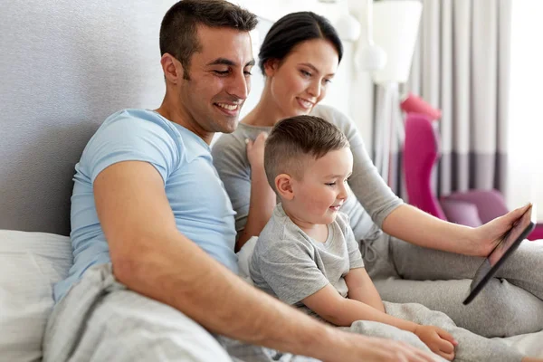 Família feliz com tablet pc na cama em casa — Fotografia de Stock