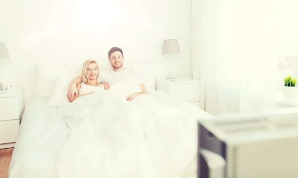 Feliz pareja acostada en la cama en casa y viendo la televisión —  Fotos de Stock