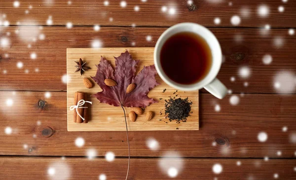 Taza de té, hoja de arce y almendra sobre tabla de madera — Foto de Stock