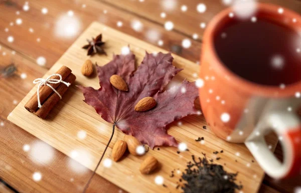 Šálek čaje, javorový list a mandle na dřevěné desce — Stock fotografie