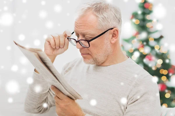 Uomo anziano in occhiali che legge il giornale a casa — Foto Stock