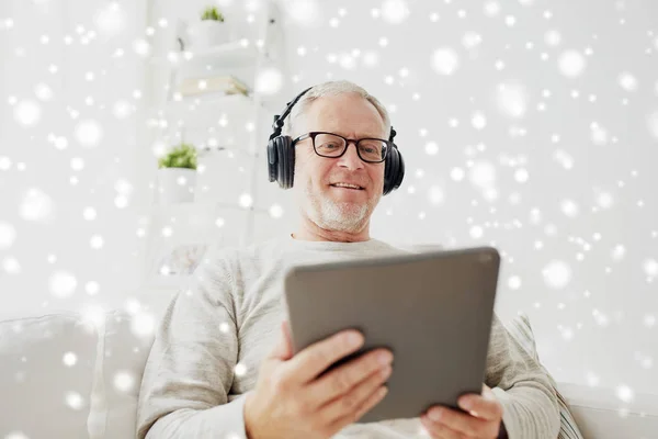 Homem idoso com tablet pc e fones de ouvido em casa — Fotografia de Stock