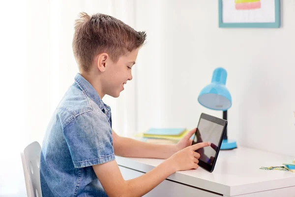 Menino sorridente com tablet pc sentado na mesa de casa — Fotografia de Stock