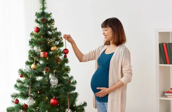 Беременная женщина украшает елку дома — стоковое фото