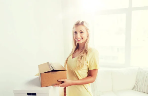 Улыбающаяся молодая женщина с картонной коробкой дома — стоковое фото