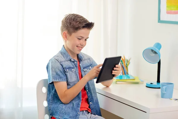 Улыбчивый мальчик с планшетным компьютером, сидящий за домашним столом — стоковое фото