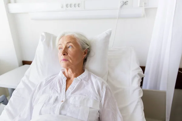 Сумна старша жінка лежить на ліжку в лікарняному палаті — стокове фото