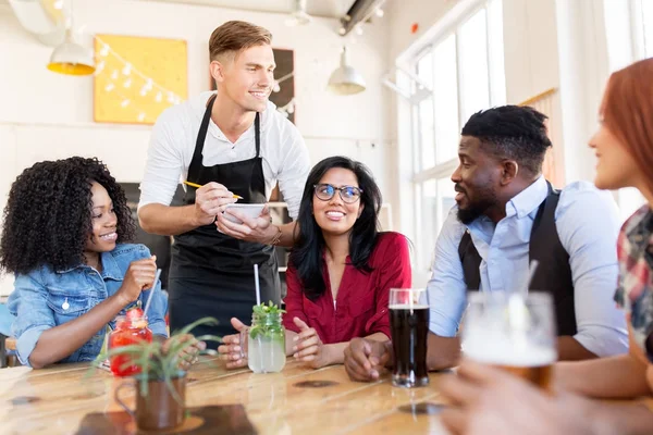 Servitör och vänner med meny och drycker i baren — Stockfoto