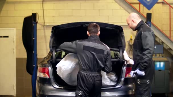 Mecánicos sacando neumáticos del maletero del coche en servicio — Vídeo de stock