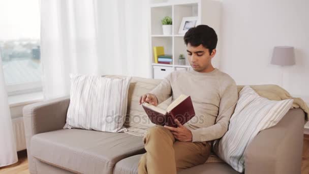 Hombre sentado en el sofá y leyendo libro en casa — Vídeo de stock