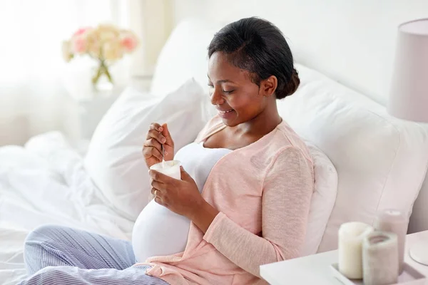 Pregnant woman eating yogurt in bed — Stock Photo, Image