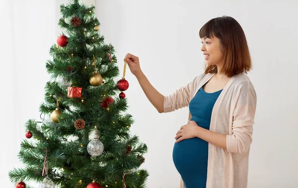 Беременная женщина украшает елку дома — стоковое фото