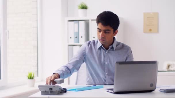 Uomo d'affari con il computer portatile che chiama al telefono in ufficio — Video Stock