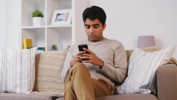 Homem com smartphone sentado no sofá em casa — Vídeo de Stock