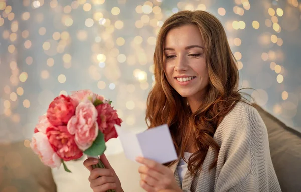 Femme heureuse avec des fleurs et carte de voeux à la maison — Photo