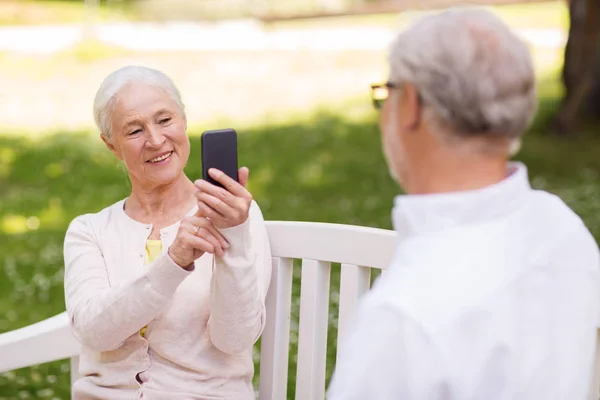 old woman photographing man by smartphone in park