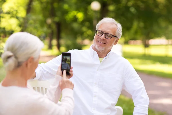Old woman photographing man by smartphone in park — Stock Photo, Image