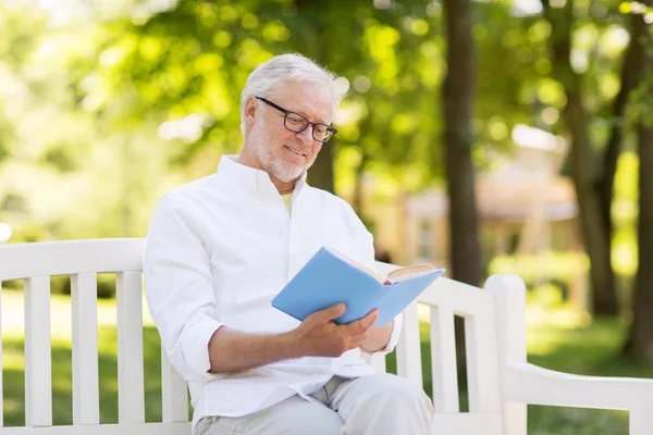 Счастливый пожилой человек, читающий книгу в летнем парке — стоковое фото