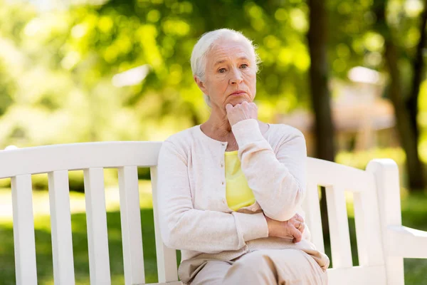 Грустная пожилая женщина сидит на скамейке в летнем парке — стоковое фото