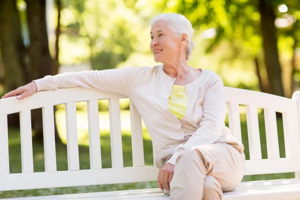 Счастливая пожилая женщина, сидящая на скамейке в летнем парке — стоковое фото