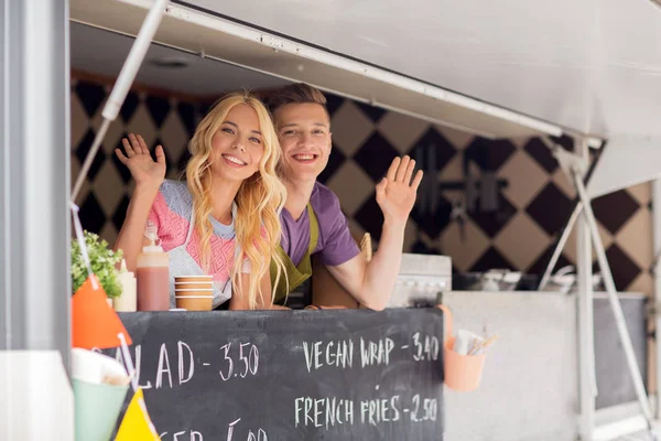 Happy young sellers waving hands at food truck — Stock Photo, Image