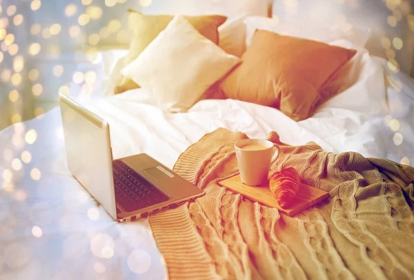 Laptop, coffee and croissant on bed at cozy home — Stock Photo, Image