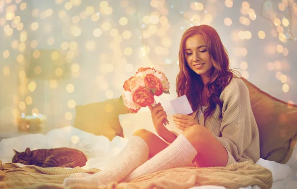 Mujer feliz con flores y tarjeta de felicitación en casa —  Fotos de Stock