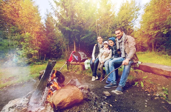 Familia feliz sentado en el banco en el fuego del campamento — Foto de Stock