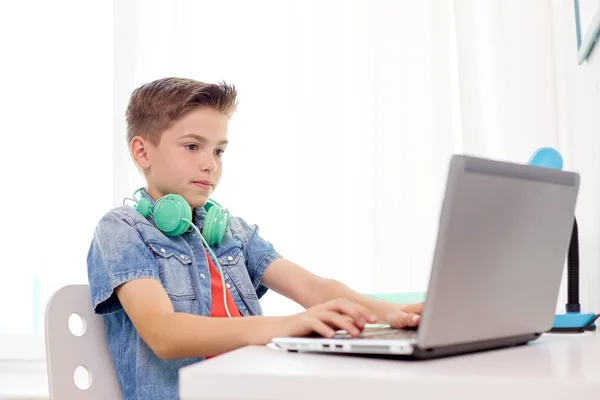 Menino feliz com fones de ouvido digitando no laptop em casa — Fotografia de Stock