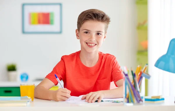 Happy student boy writing to notebook at home — Stock Photo, Image