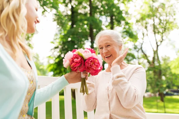 Dotter att ge blommor till senior mor på park — Stockfoto