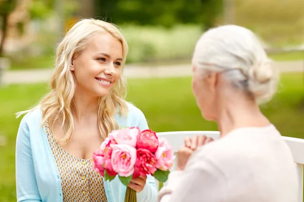 Dotter att ge blommor till senior mor på park — Stockfoto