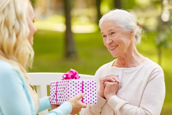 Hija dando regalo a la madre mayor en el parque — Foto de Stock